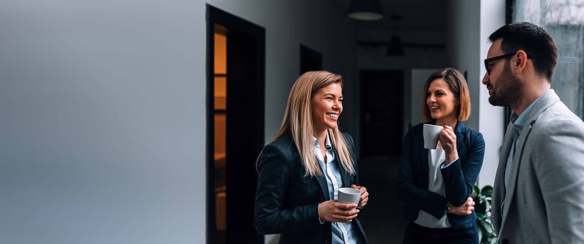 Three professionals engaging in conversation, smiling, and holding coffee cups in a modern office hallway, reflecting a collaborative work environment related to security solutions.
